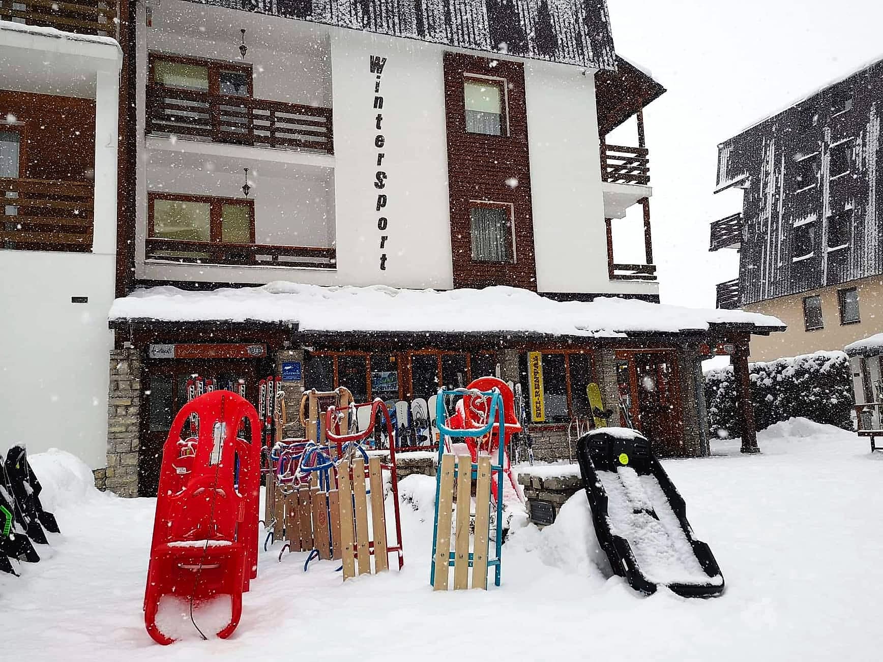 Fasada objekta WinterSport zatrpana snijegom, ispred ulaza sanke i skije