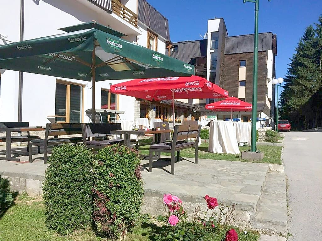 Ljetna terasa sa suncobranom i drvenim stolovima ispred objekta WinterSport